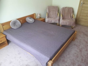 Un lit simple avec un cadre en bois et un matelas gris, deux tables de chevet avec des lampes, et deux chaises dans la pièce.