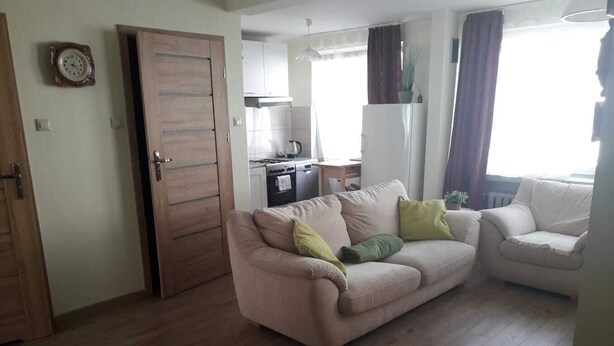A living room with a sofa, a dining area with a table and chairs, a kitchen with appliances, and a door. - Serce Gdyni by Grand Apartments (Gdynia)