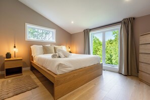 Een slaapkamer met een houten bed, een nachtkastje, een raam en uitzicht op groen.