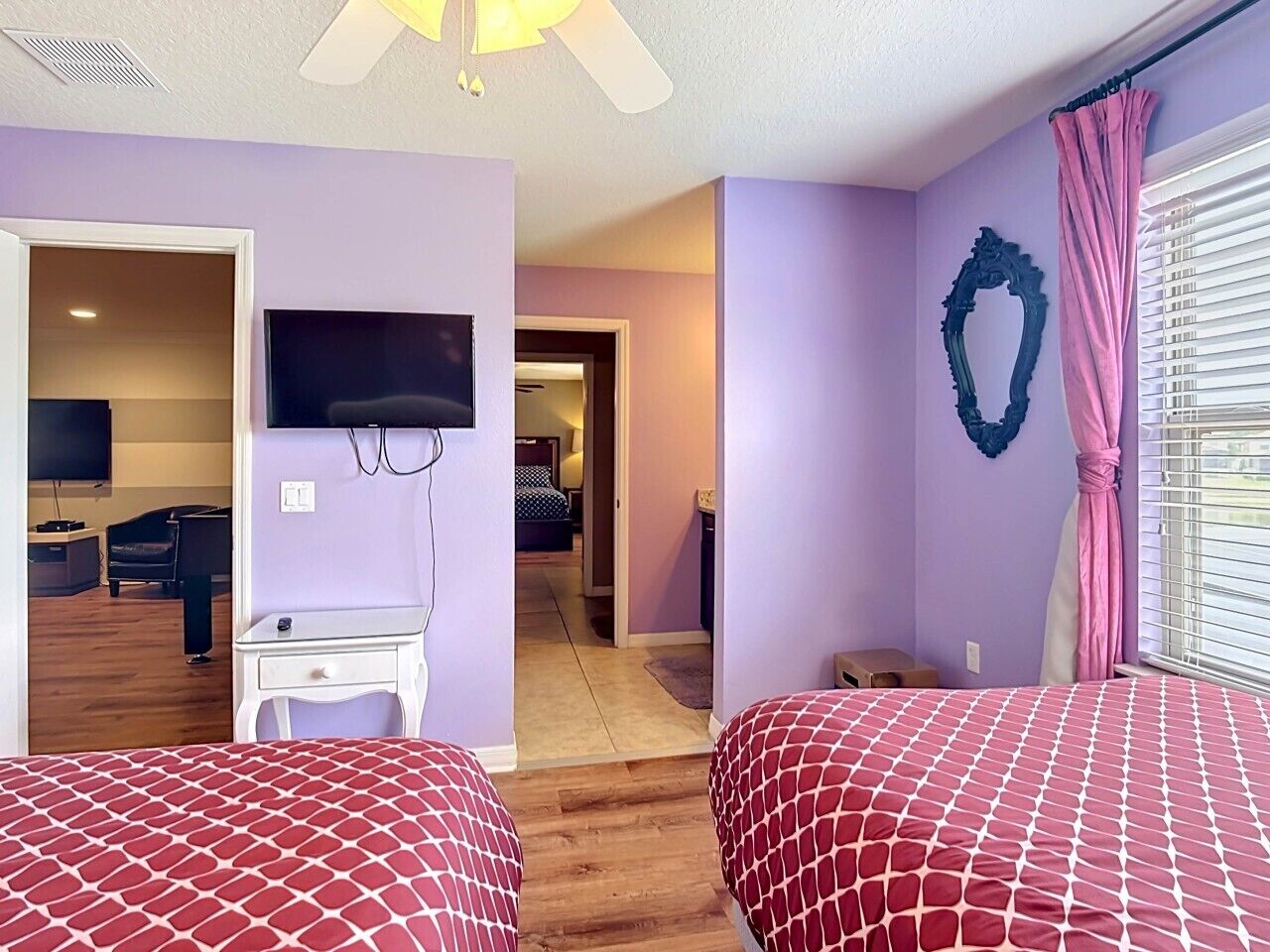 A bedroom with two beds, a desk, a TV, and a window with blinds.