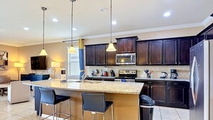 A modern kitchen with dark cabinets, a central island with bar stools, a microwave, stove, and a refrigerator. - 8BR Villa, Private Pool & Water Slides (Kissimmee)