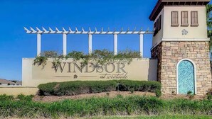 A sign for 'Windsor at Westside' with a pergola structure above it, a stone building with a blue-tiled window, and well-maintained landscaping. - Windsor Westside Beautiful 8BR Villa with Pool/Spa (Kissimmee)