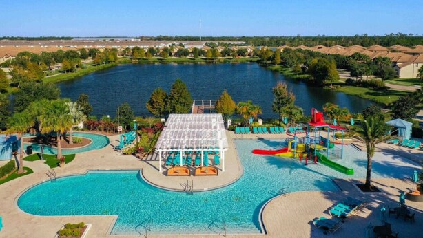 A swimming pool with a water slide, lounge chairs, and a covered area. - Windsor Westside Beautiful 8BR Villa with Pool/Spa (Kissimmee)