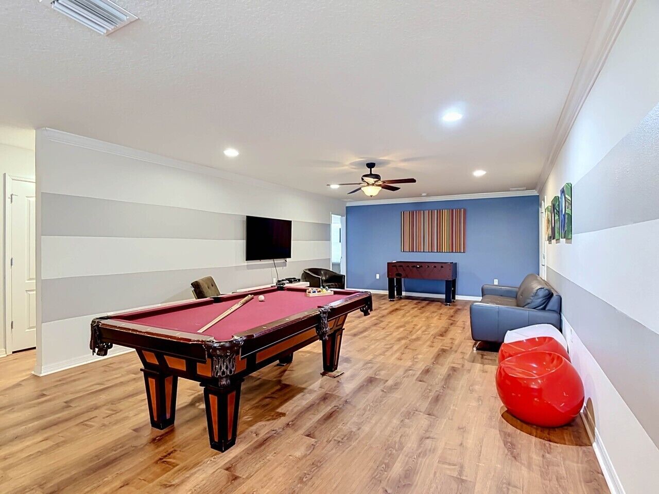Quarto com mesa de bilhar, ventoinha no teto, sofá e um puff vermelho.