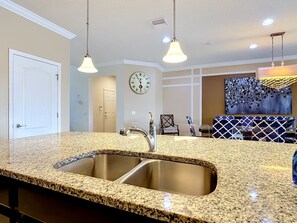 A kitchen with granite countertops, stainless steel sink, pendant lights, and a clock on the wall. - Luxury 8BR Lake View Villa Near Disney with Pool (Kissimmee)