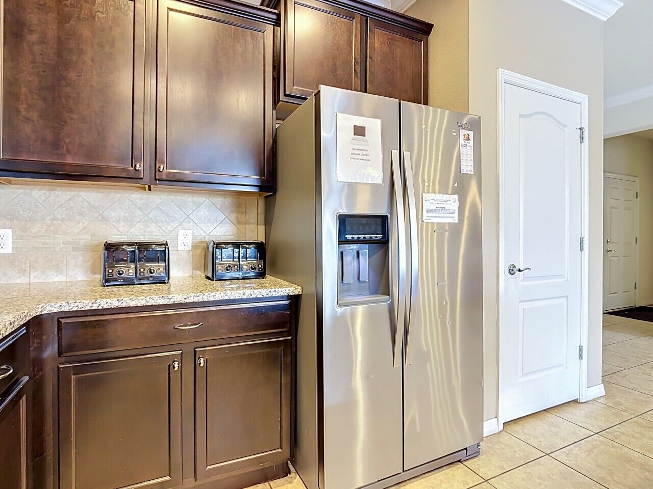 A kitchen with dark wooden cabinets, a stainless steel refrigerator, and a microwave.