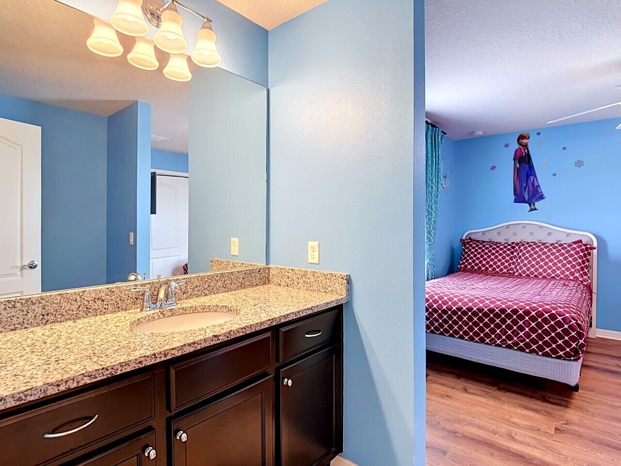 Un baño con lavamanos de encimera de granito, muebles oscuros y un espejo.