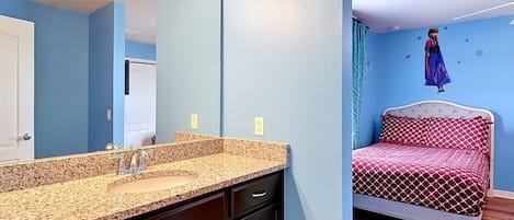 Un baño con lavamanos de encimera de granito, muebles oscuros y un espejo.