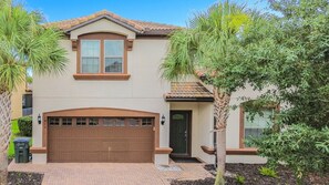 A two-story house with a brown garage door, a front door, and a small porch area. - 8BR Villa with Pool & Spa, Near Disney (Kissimmee)