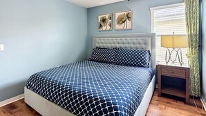 Quarto com cama, ventilador de teto, mesa de cabeceira com abajur e dois quadros de flores na parede.
