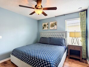 A bedroom with a bed, a ceiling fan, a nightstand with a lamp, and two wall-mounted flower paintings. - 8BR Villa with Pool & Spa, Near Disney (Kissimmee)