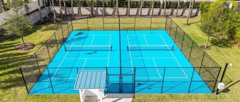 A tennis court with a net, surrounded by a fence, and a small white structure in the center.