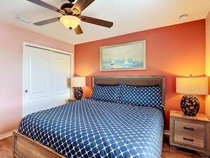 A bedroom with a bed, a ceiling fan, a nightstand with a lamp, and a painting on the wall. - 8BR Villa with Pool & Spa, Near Disney (Kissimmee)