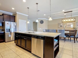 A modern kitchen with stainless steel appliances, a granite countertop, pendant lighting, and a dining area with patterned chairs. - 8BR Villa with Pool & Spa, Near Disney (Kissimmee)