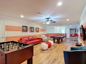 A room with a foosball table, a pool table, a red sofa, and a ceiling fan. - 8BR Villa with Pool & Spa, Near Disney (Kissimmee)