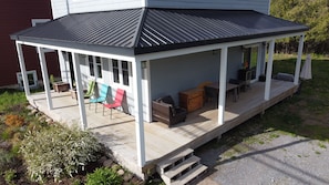Een overdekt terras met stoelen en tafels, een houten terras en een huis op de achtergrond.