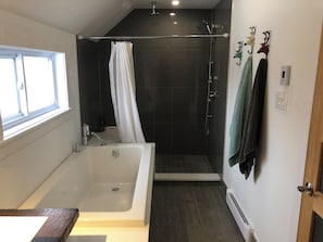 Een moderne badkamer met een bad, douche en een raam.