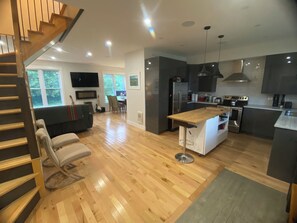 Een moderne keuken met een centraal eiland, een zithoek met een bank en stoelen, een trap en een aan de muur bevestigde televisie.