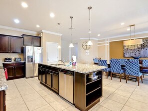 A modern kitchen with a central island, built-in appliances, and a dining area with patterned chairs. - Windsor at Westside 8BR + Water Slide, Near Disney (Kissimmee)