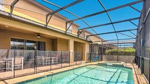 Ein Schwimmbecken mit überdachtem Bereich, Liegestühlen und Blick auf ein Gebäude mit Balkon.