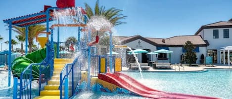A water park with slides and a pool, surrounded by buildings with outdoor seating.