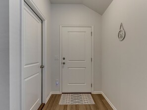Un pasillo con una puerta blanca, un tapete estampado y una lámpara fijada a la pared.