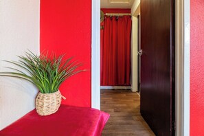 Um corredor com parede vermelha, piso de madeira e porta que dá para outro cômodo.