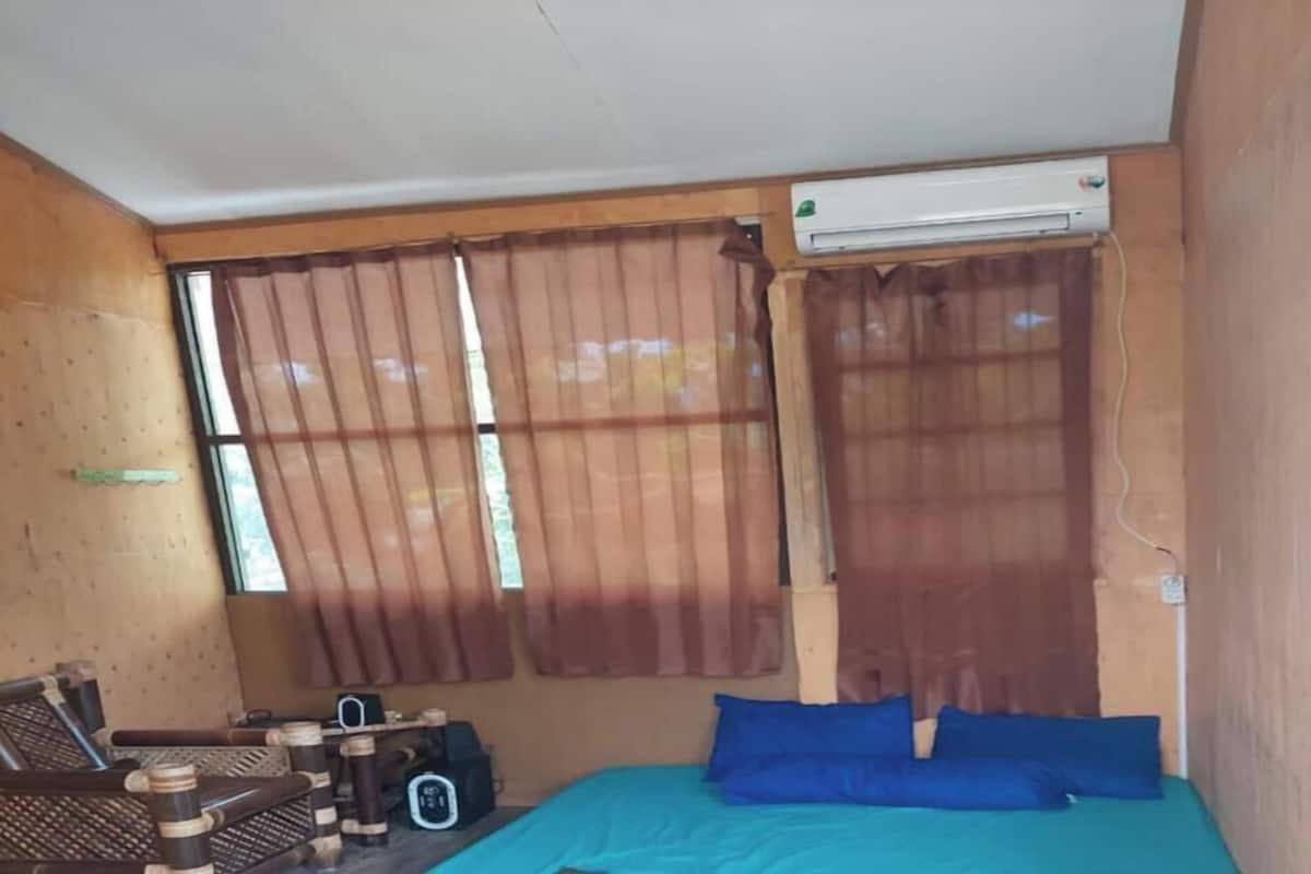 A room with a bed, a window with curtains, a wall-mounted air conditioner, and a small table with a chair.