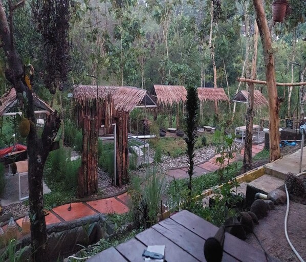 A tropical garden with thatched-roof structures, a stone pathway, and wooden benches.