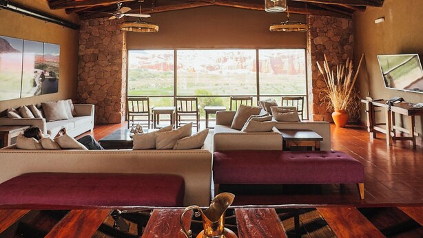 A spacious room with a large wooden ceiling, multiple hanging light fixtures, a stone wall, and a view through large windows.