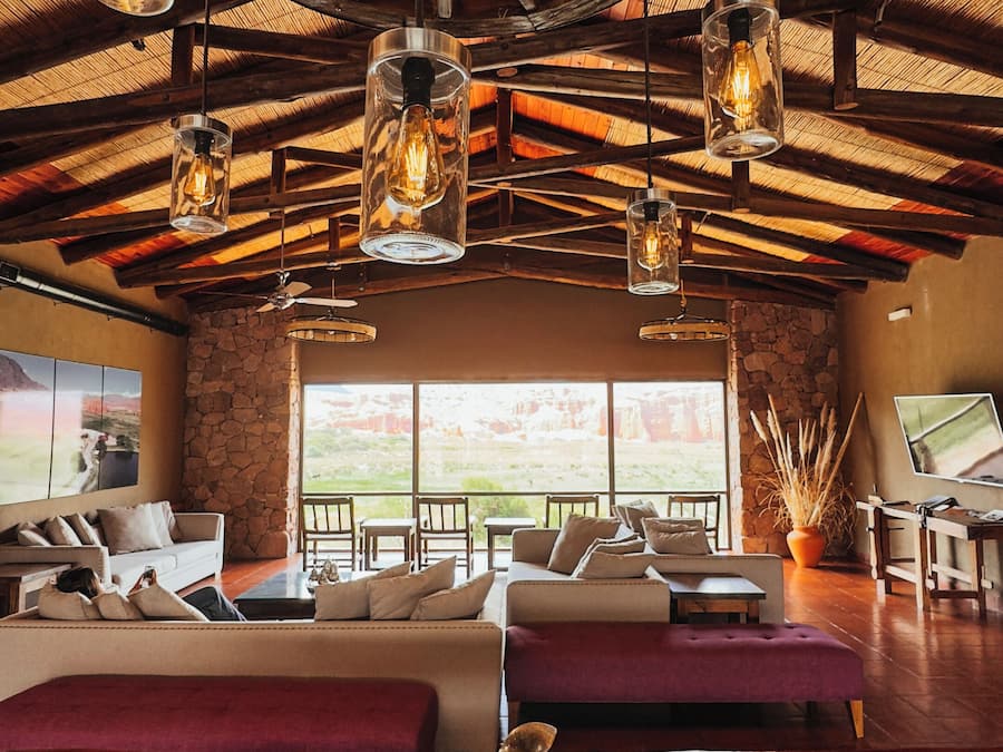 Una habitación amplia con un gran techo de madera, varias lámparas colgantes, una pared de piedra y vistas a través de amplios ventanales.