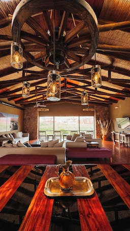 A spacious room with a large wooden ceiling, multiple hanging light fixtures, a stone wall, and a view through large windows.
