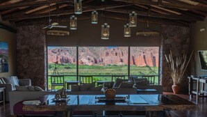 A rustic interior with a large wooden table, stone walls, and a view of red rock formations.