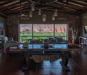 A rustic interior with a large wooden table, stone walls, and a view of red rock formations. - Hotel Castillos De Cafayate (Cafayate)