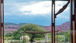 A covered outdoor area with a pool, stone flooring, lounge chairs, and a view of mountains.