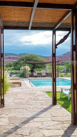 A covered outdoor area with a pool, stone flooring, lounge chairs, and a view of mountains. - Hotel Castillos De Cafayate (Cafayate)