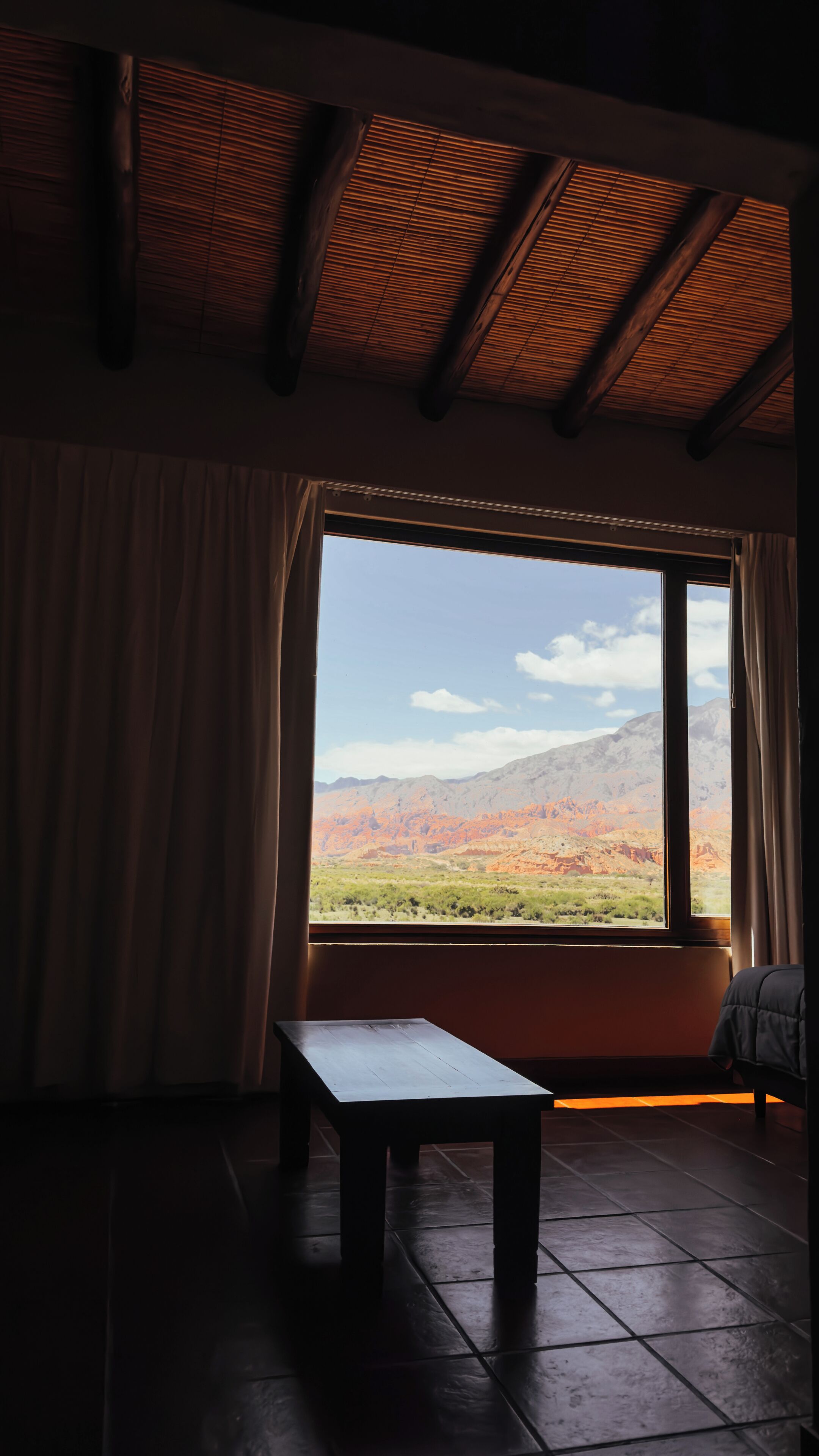 Una habitación con un ventanal grande, un banco de madera y vistas a un paisaje montañoso.