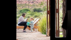 A room with a view of a desert landscape, a wooden bench, and a doorway leading outside.