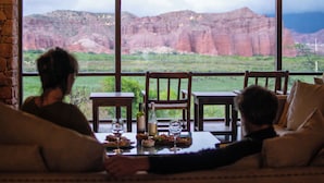 A dining area with a table set for two, a view of red rock formations, and a brick wall.
