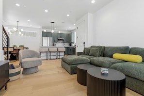A modern living room with a grey sofa, ottoman, and a black coffee table. A staircase with a railing is visible in the background. - Chic 3BR in East Austin w EV Charger, Near DT! (Austin)