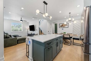 A modern kitchen with a central island, built-in appliances, and a dining area with a table and chairs. - Chic 3BR in East Austin w EV Charger, Near DT! (Austin)