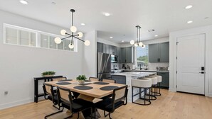 Een moderne keuken met grijze kastjes, een centraal eiland en een eethoek met een ronde tafel en stoelen.