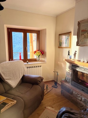 Ein Wohnzimmer mit Sofa, Kamin, einem Vorhangfenster und einer Vase mit Blumen.