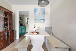 A dining area with a white table, wooden cabinets, and a painting of a seascape. - Stay Here! | Next to Shem Creek | Minutes from CHS (Mount Pleasant)