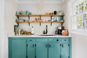 A kitchen with teal cabinets, wooden shelves, and a window with a view of trees. - Stay Here! | Next to Shem Creek | Minutes from CHS (Mount Pleasant)
