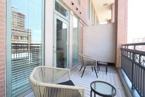 Ein Balkon mit Korbstühlen, einem kleinen runden Tisch und einer Glastür zu einem Innenbereich.
