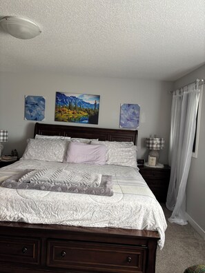 A bedroom with a bed, a nightstand, a lamp, and three paintings on the wall.