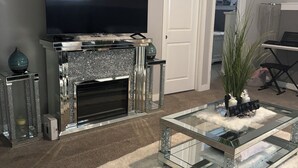 A living room with a flat-screen TV, a fireplace, a glass coffee table, and a white door. - Beautiful, quiet, clean, cozy and affordable house to host at least 10 guest. (Grande Prairie)