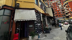 Straßenansicht mit einem gelben Gebäude, einem Friseursalon und einem mehrstöckigen Wohnhaus.