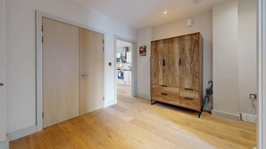 A hallway with wooden flooring, a wardrobe, and a door leading to a kitchen. - Bright 2BR Home w/ Private Garden Near Wimbledon (London)